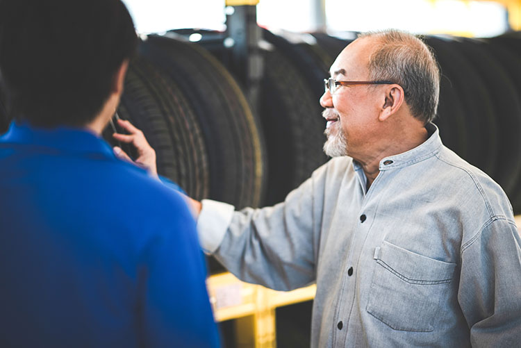 A customer consulting with a specialist about tires in a tire shop, with many tires displayed in the background.