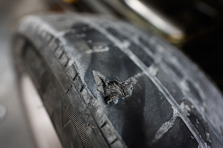 Close-up of a damaged tire showing a bulge and visible wear, indicating the need to replace the tires.