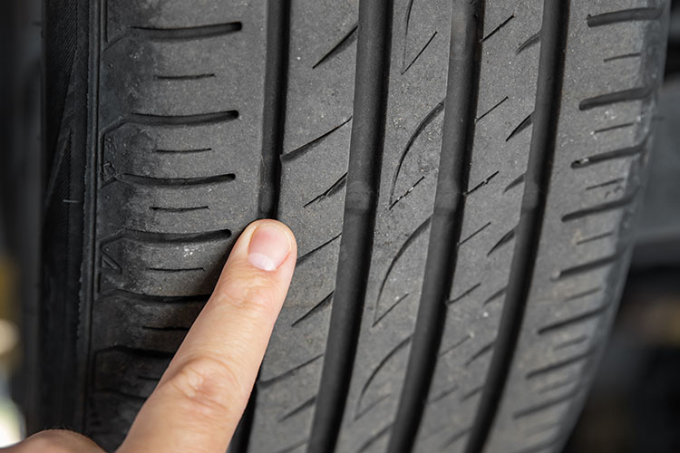 Close-up of a hand inspecting the tire tread to check for signs of worn tires.