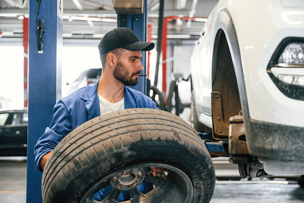 Mechanic performing a tire rotation in an auto repair shop, inspecting a tire before installation.