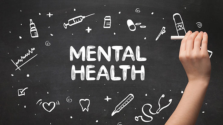 The words “mental health” are seen written in white on a black chalkboard beside a hand with chalk with white images of teeth, medical devices, teeth, hearts, and checkboxes surrounding the text. 