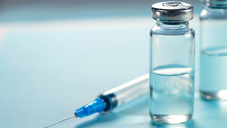 A syringe rests on a light blue surface next to two glass bottles filled with liquid.