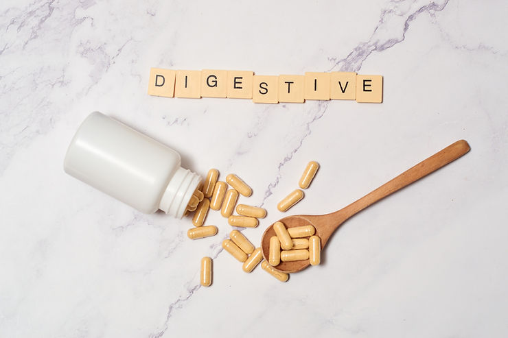 The word “digestive” is spelled out in letter tiles next to a scatter of vitamins falling out of a bottle against a marble background. 