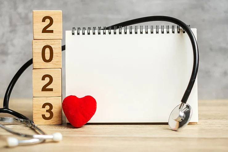 Four wooden blocks spelling out 2023 beside a blank pad of paper, a stethoscope, and a small red heart.