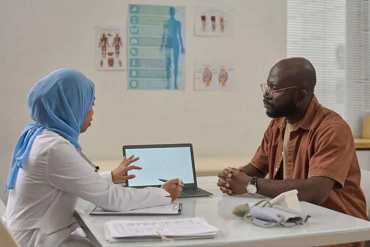 A female physician explains the diagnostic results on a laptop to her attentive Black male patient.