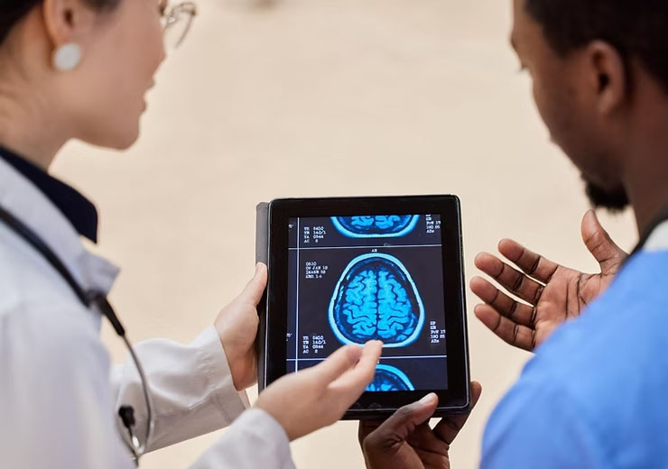 An X-ray of a brain with a doctor and nurse in a hospital, discussing the diagnosis while examining brain scan results on a tablet.