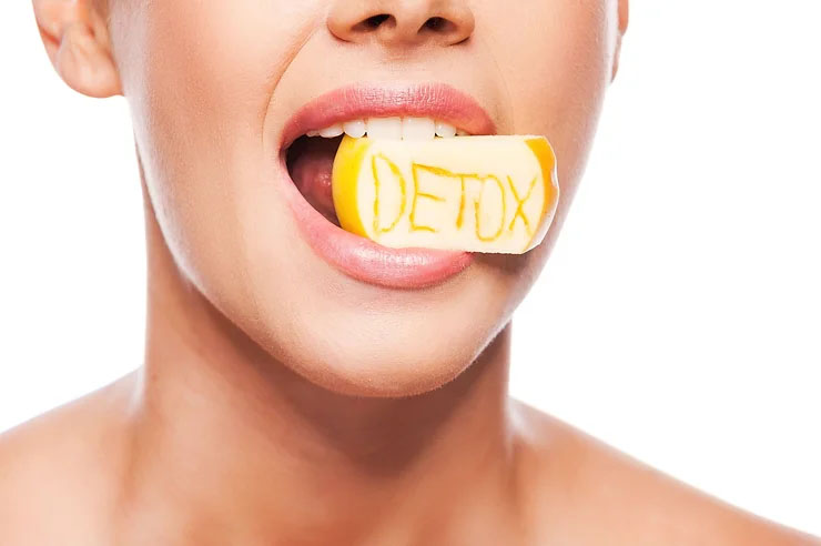 A female model holds a wedge of apple in her mouth. The word “detox” is carved into the apple.