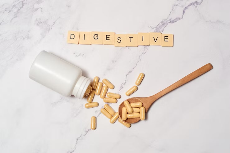 The word “digestive” is spelled out in letter tiles next to a scatter of vitamins falling out of a bottle against a marble background.