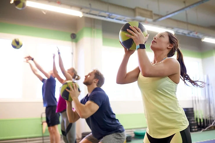 Four people train with a medicine ball in a gym, working together to enhance their fitness and strength.