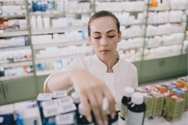 A diligent pharmacist at work, picking out a prescription bottle from a shelf filled with medications in a pharmacy.