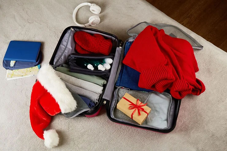 An open suitcase packed with neatly folded clothes, travel documents, a wrapped gift, a Santa Claus hat, and various toiletries.
