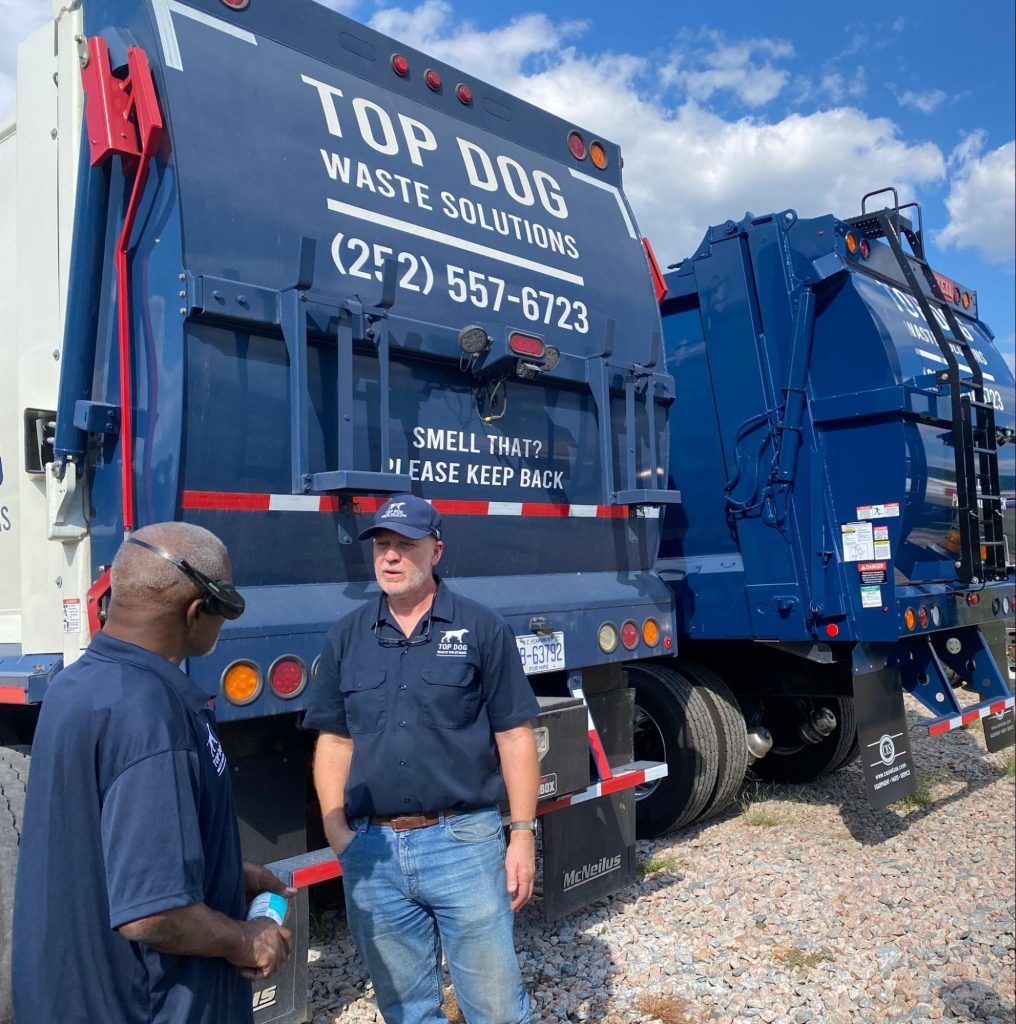 Two men next to waste removal trucks.