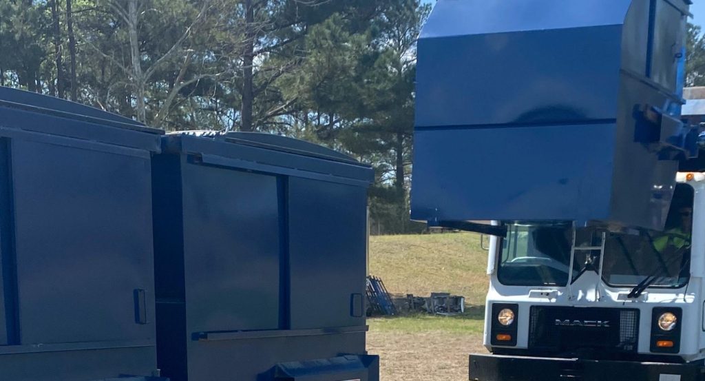 Waste removal truck next to dumpsters.