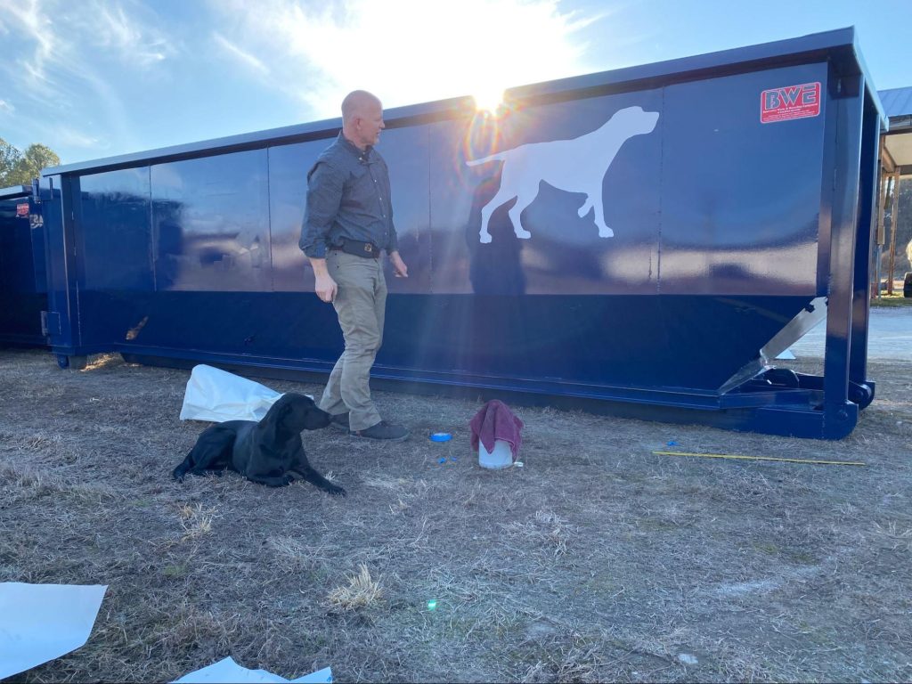 Man and a dog next to a dumpster.