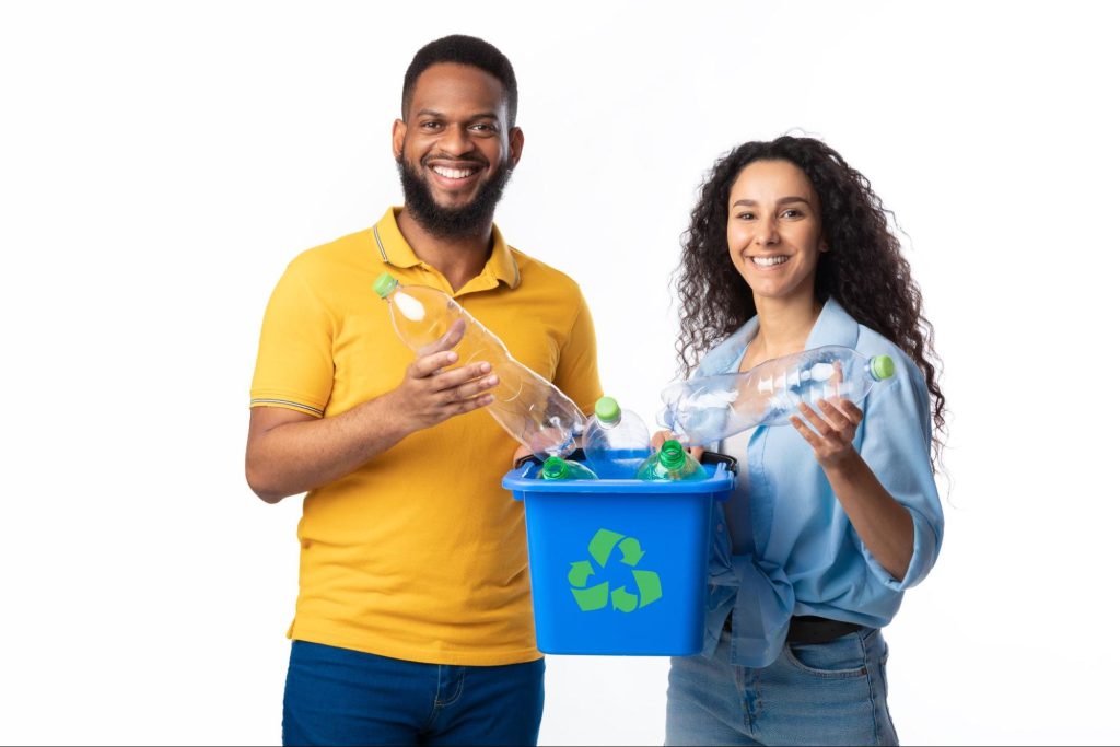 A happy couple holds plastic bottles and a full recycling bin.