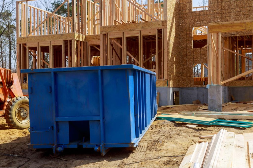 A blue dumpster near the apartment building construction site with a red tractor on the left side.